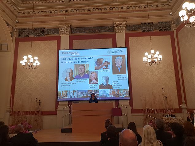 Donata Romizi bei Ihrer Rede; im Hintergrund Präsentationsfolie mit Bildern von Lehrenden des ULG